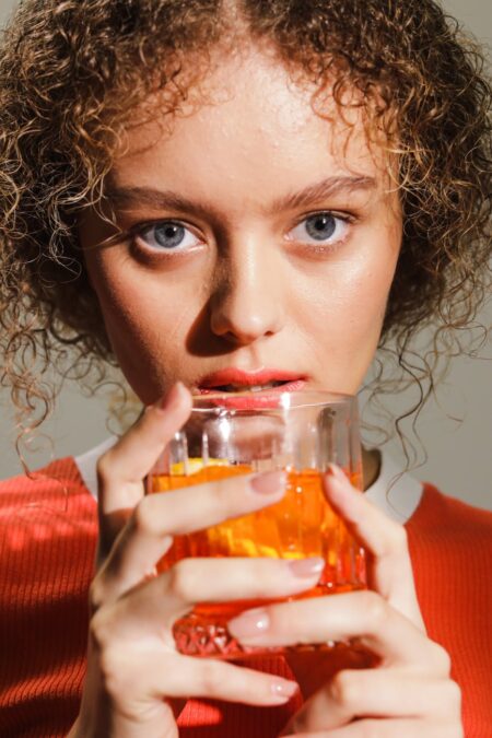 a woman with curly hair holding a negroni cocktail